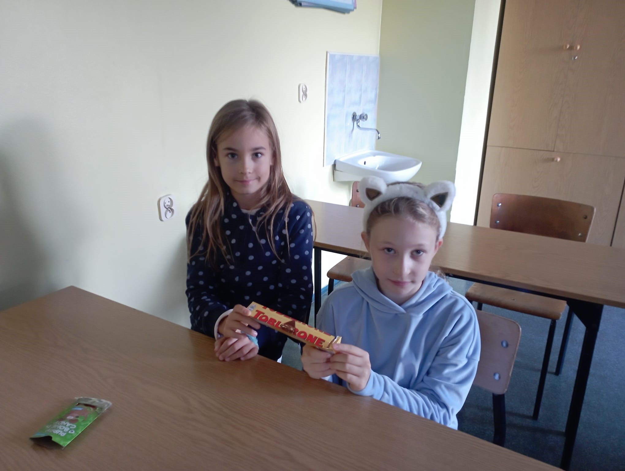 Uczennice siedzą w ławce i pokazują szwajcarskie smakołyki