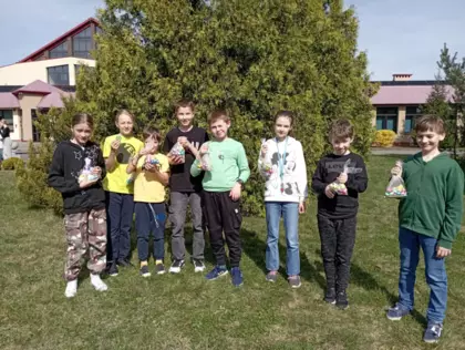 Uczniowie stoja na tle zieleni, trzymają w rękach woreczki z czekoladowymi jajkami. 