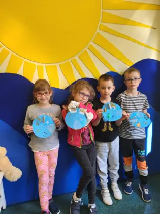 Uczniowie stoja w sali lekcyjnej i prezentują wykonane przez siebie wycinanki z cyklem  rozwojowym żaby