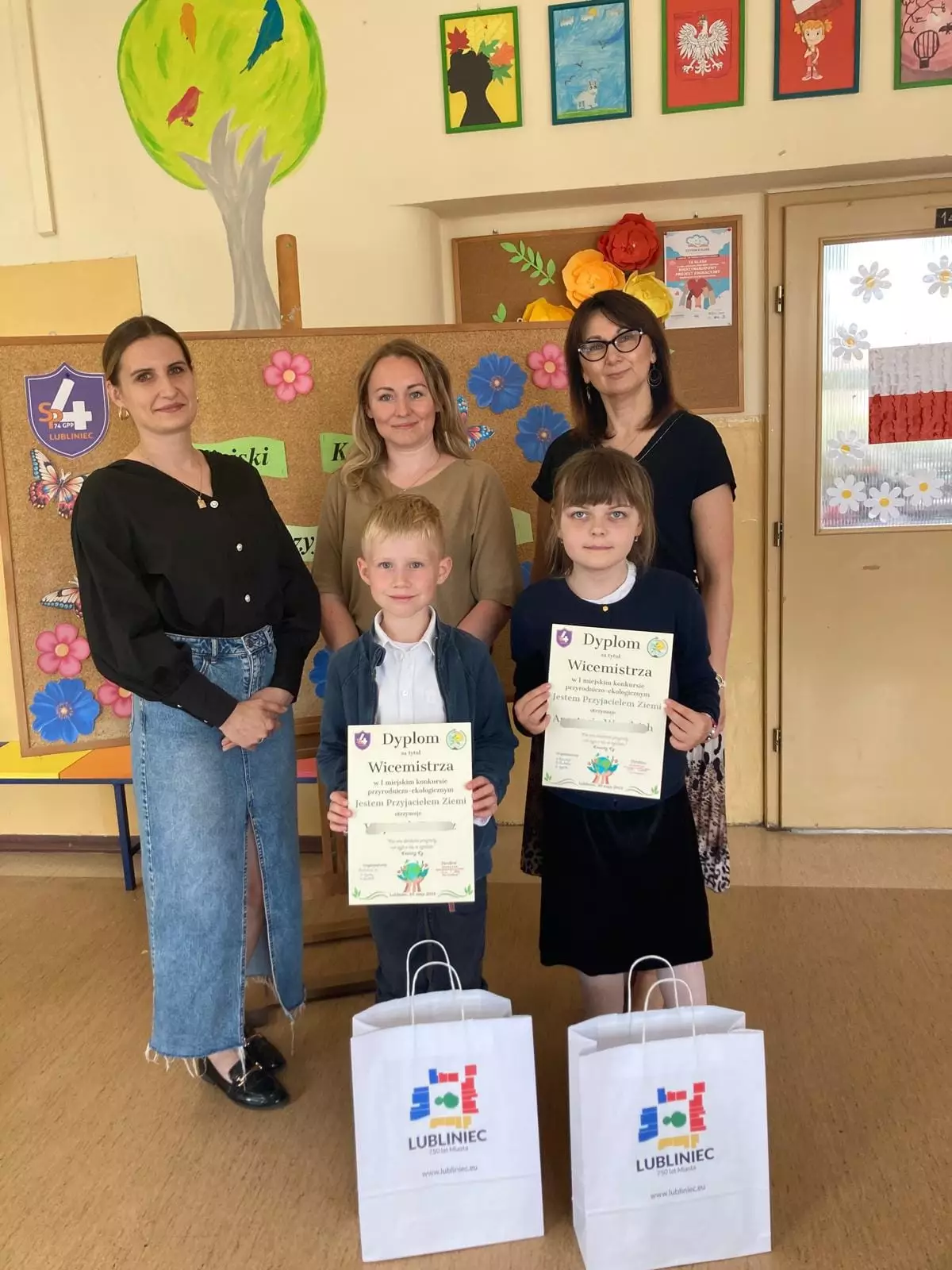 Uczniowie którzy trzymają dyplomy, za nimi trzy nauczycielki